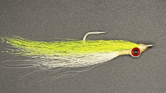 A fly fishing lure with a bright chartreuse yellow-green body, a white skirt, and a red-and-black eye, shown on a dark gray textured background.
